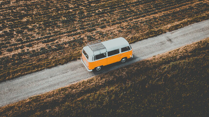 Volkswagen Van combi vw t2 - vanlife - une vue aérienne d'une camionnette de style vintage orange et blanche circulant sur une route à travers ce qui semble être une zone sèche