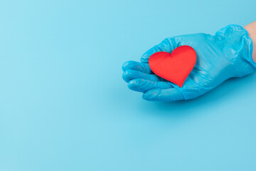 Red heart in hands in blue medical gloves on blue background. Background for the day of the medic. World Heart Day. Heart diseases.