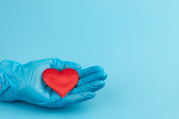 Red heart in hands in blue medical gloves on blue background. Background for the day of the medic. World Heart Day. Heart diseases.