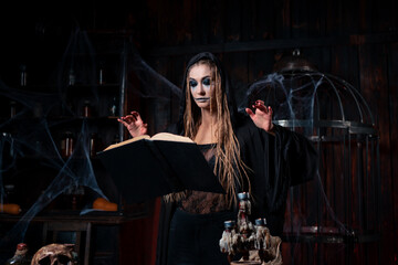 Halloween concept. Witch dressed black hood with dreadlocks standing dark dungeon room use magic book for conjuring magic spell - obrazy, fototapety, plakaty