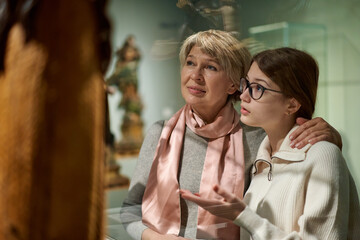 Attentive tween girl with senior woman exploring art museum