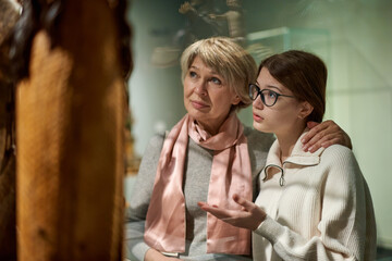 Girl with woman looking with interest at art objects under glass in museum