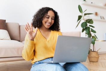 Cheerful young African American woman making video call on laptop at home, waving at webcam