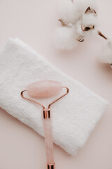 Jade face roller with towel on a pink background, face care concept. Vertical image
