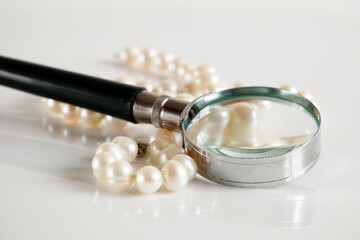 Fototapeta na wymiar pearls necklace and magnifying glass on white backgrond, pawnshop concept