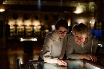 Attentive tween girl with senior woman exploring art museum