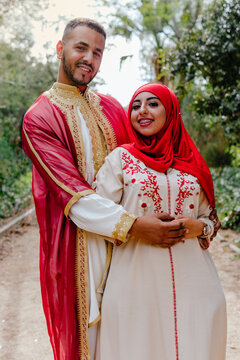 Young arabian couple with traditional clothes embraced and looking at the camera in a green space.