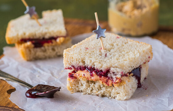 Snack or lunch, sandwiches on white bread with peanut butter and jam on a wooden board on a green concrete background. Classic sandwich recipes.