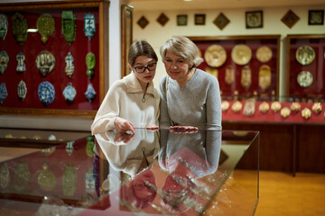 Teenage girl and mature woman observing exhibition in historical museum