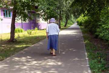 Fototapeta na wymiar An elderly woman with a cane walks around the city.