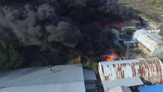 Severe fire in the warehouse. Black smoke in the sky. The drone is filming a large-scale fire. Rescuers put out the fire.