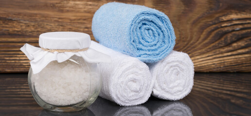 Obraz na płótnie Canvas on a dark wooden background, a towel wrapped in a roll and white bath salt in a glass jar, for relaxation
