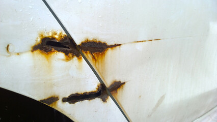Sheet metal corrosion of old white car body. Rusty dirty steel surface, background and damaged texture. Stops and prevents rust. Used vehicles service. Professional paint and repair. Messy. Coat.
