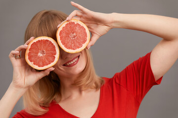 Beautiful woman with citrus fruits in hands at the eyes. Model with long hair hold cut grapefruit in hands as glasses isolated on gray. Skin care concept. Healthcare concept.