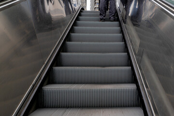 Low angle of a man standing on step of escalator in subway or metro, Vertical transportation in the form of a moving staircase which carries people between floors of a building.