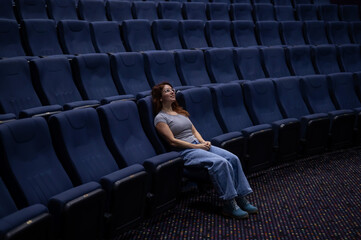 Caucasian red-haired woman sits on the front row in a cinema in an empty hall. The girl is watching...