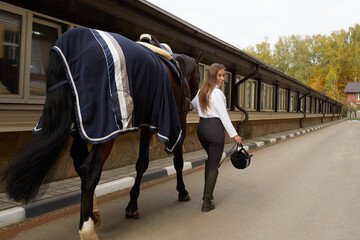 Female horseman going with her brown horse outdoor. Concept of animal care. Rural rest and leisure. Idea of green tourism. Young european woman wearing helmet and uniform