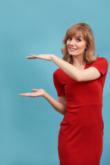 Young beautiful blonde woman wearing stylish red dress making frame with her hands on a blue wall background. Copy, empty space for text