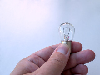 A hand of a man holding small light bulb for car