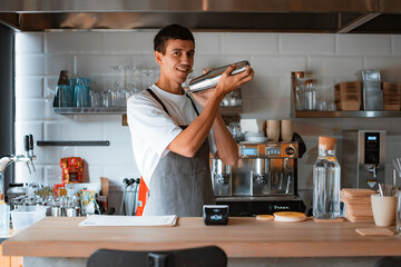 Smiling professional male barista making caramel iced frappe while working in local coffee shop