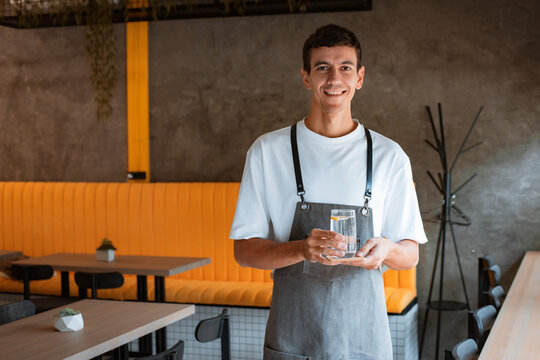 Young Pleasant Man Cafe Worker In Apron Serving Table In Local Stylish Coffeehouse Or Coffee Shop