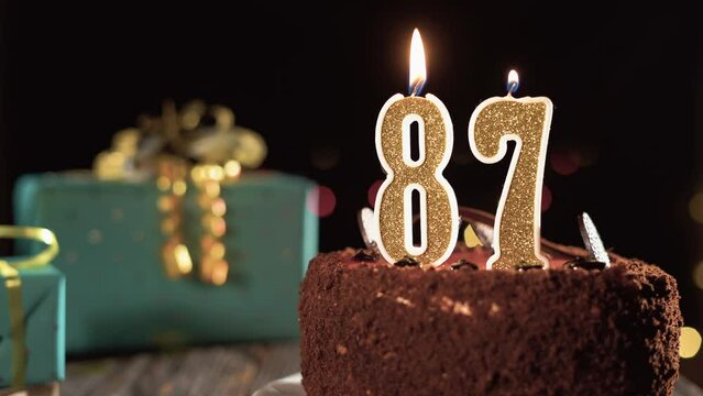 Number eighty seven birthday candle on sweet cake on the table, 87th birthday. Fire from the lighter, blow out the holiday candle.