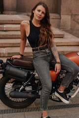 Obraz na płótnie Canvas Fashion woman biker posing on retro style motorcycle outdoors