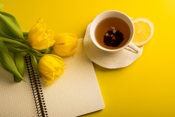 Yellow tulips with cup of tea, notepad on yellow