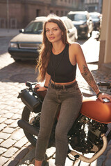 Brown haired woman posing with urban retro motorbike on alley