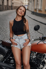 Tattooed female motorcyclist posing with retro bike outdoors