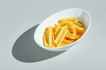 French fries in white bowl on light background. Hard light, deep shadow