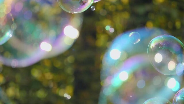 Slow-motion shot of colorful soap bubbles reflecting the sun with gorgeous sun rays and flares
