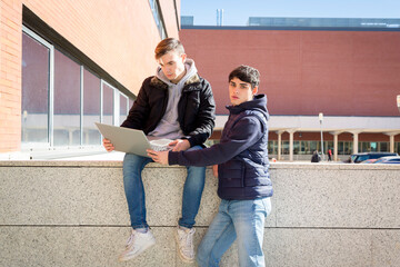 couple of university students, one sitting and the other standing with laptop computer