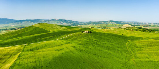 Stunning aerial view of green fields and farmlands with small villages on the horizon. Rural landscape of rolling hills, curved roads and cypresses of Tuscany, Italy.