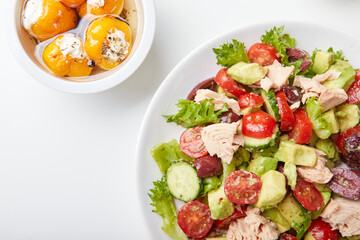 Salad with tuna, lettuce, cucumbers, tomatoes, olives and avocados in white plate on the table