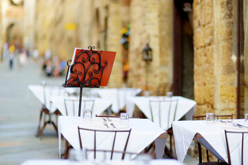 Outdoor cafe table in medieval San Gimignano hill town, famous for its skyline of medieval towers, including the stone Torre Grossa. Province of Siena, Tuscany, Italy. - obrazy, fototapety, plakaty
