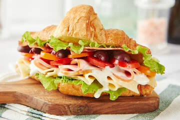 Croissant sandwich with cheese, ham, lettuce, tomatoes, olives and delicious sauce on wooden board.