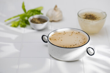 Healthy bone broth with spices in bowl on a white tile with a shadow pattern. The concept of keto diet and paleo diet. 