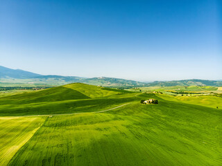 Stunning aerial view of green fields and farmlands with small villages on the horizon. Rural landscape of rolling hills, curved roads and cypresses of Tuscany, Italy.