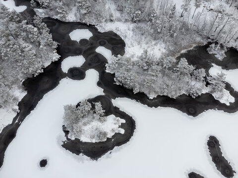Aerial, drone photography of lake with partly frozen ice in winter season in Sweden. Bird's eye view of trees, snow, thin ice and water. Copy space and place for text.