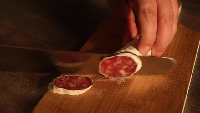 Full HD video clip of 10 seconds of duration in the process of cutting a fuet sausage on a wooden board.