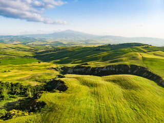 Stunning aerial view of green fields and farmlands with small villages on the horizon. Rural landscape of rolling hills, curved roads and cypresses of Tuscany, Italy.