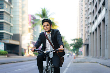 Fototapeta na wymiar Asian businessman in a suit is riding a bicycle on the city streets for his morning commute to work. Eco Transportation Concept..