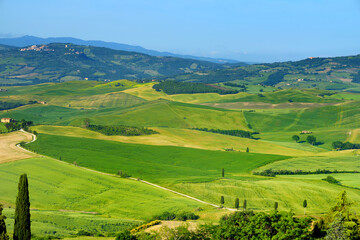 Stunning view of green fields and farmlands with small villages on the horizon. Rural landscape of rolling hills, curved roads and cypresses of Tuscany, Italy.