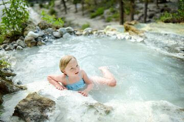 Young girl bathing in Bagni San Filippo, small hot spring containing calcium carbonate deposits, forming white concretions and waterfalls. Geothermal pools and hot springs in Tuscany, Italy.
