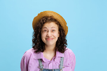 Emotional young beautiful curly girl wearing plaid shirt and hat making faces isolated on blue background. Concept of funny meme emotions