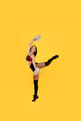 Beautiful cheerleader in costume holding pom poms on yellow background
