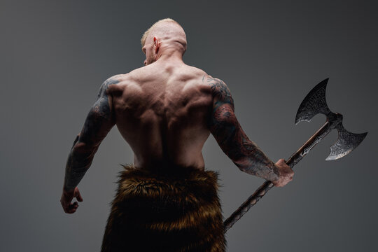 Tattooed viking with steel axe his back facing to camera
