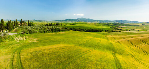 Stunning view of fields and farmlands with small villages on the horizon. Summer rural landscape of rolling hills, curved roads and cypresses of Tuscany, Italy.