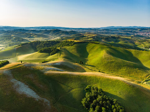Stunning aerial view of green fields and farmlands with small villages on the horizon. Rural landscape of rolling hills, curved roads and cypresses of Tuscany, Italy. - Powered by Adobe